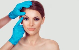 medically gloved hands touching patient’s eyebrow