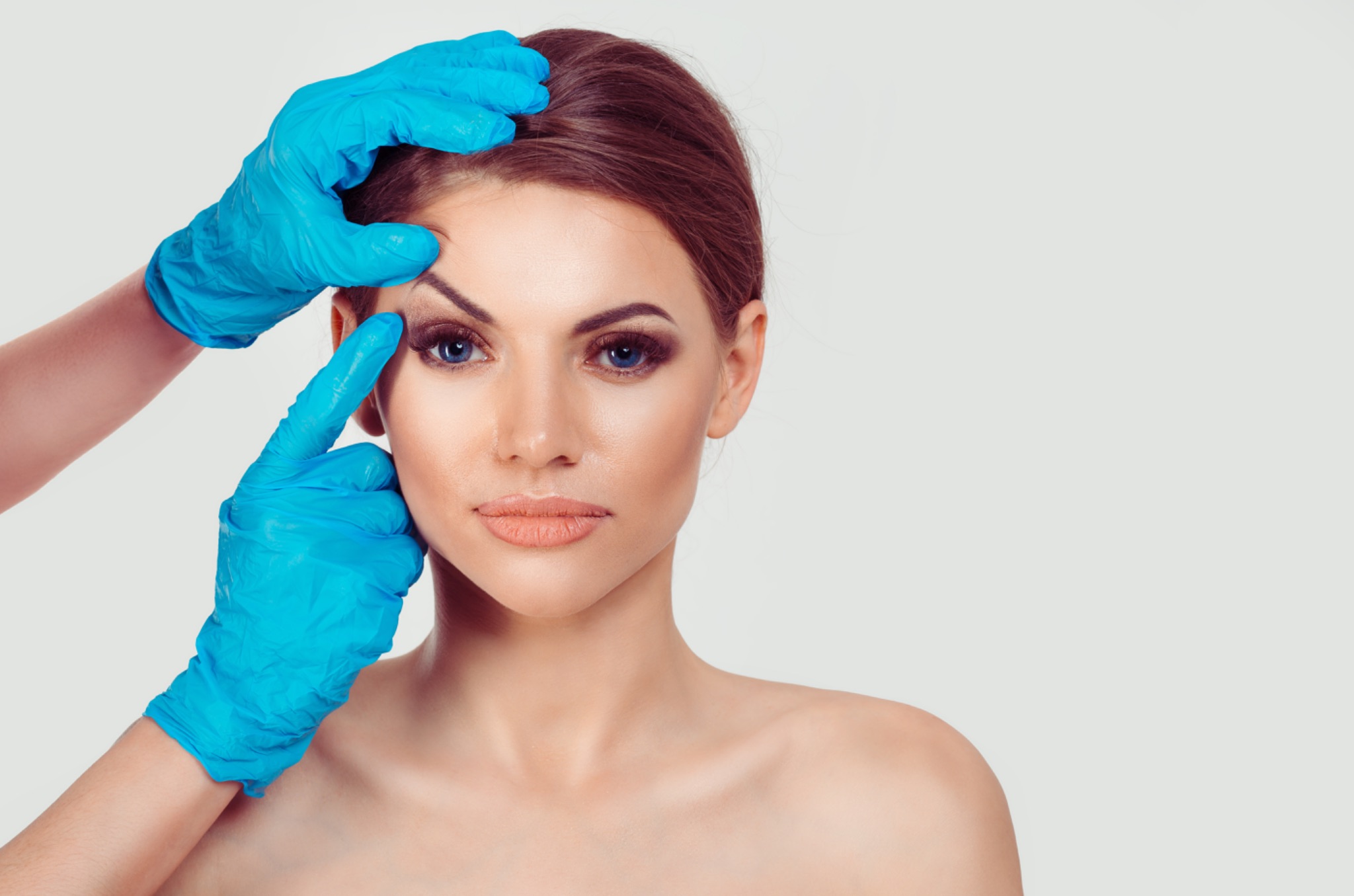 medically gloved hands touching patient’s eyebrow
